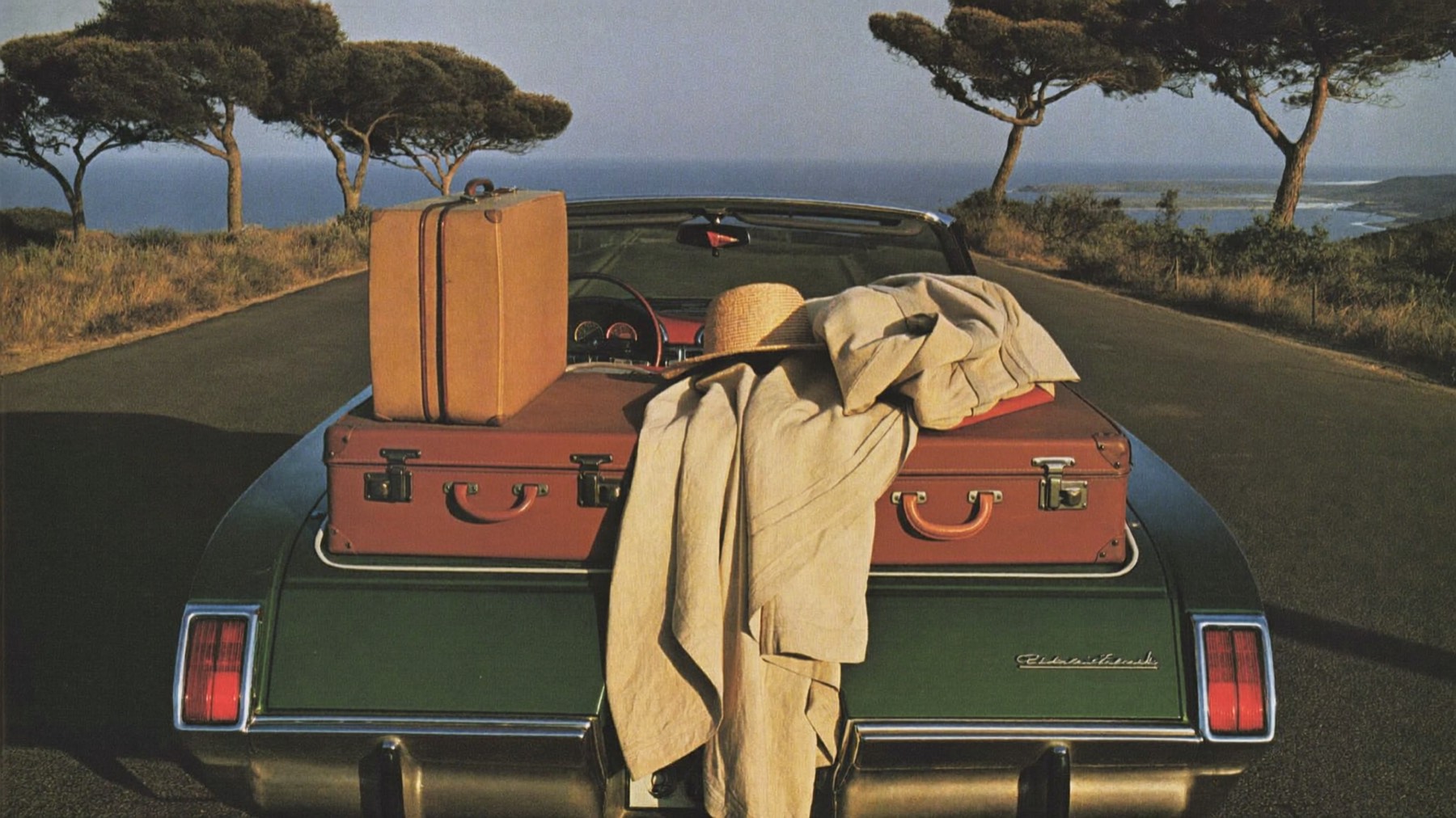 Leather suitcases and a linen coat in the open trunk of a vintage car by the sea